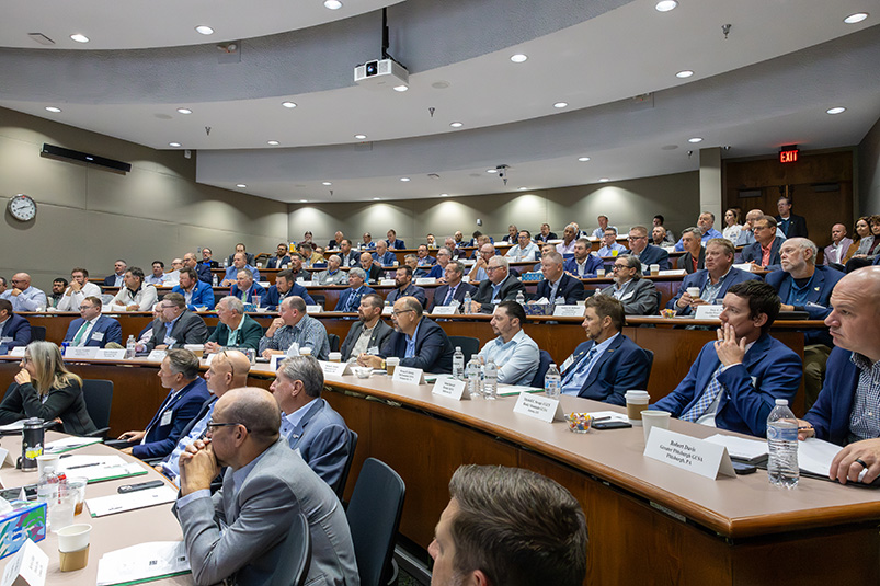 a large group of men sitting inside a tiered conference room