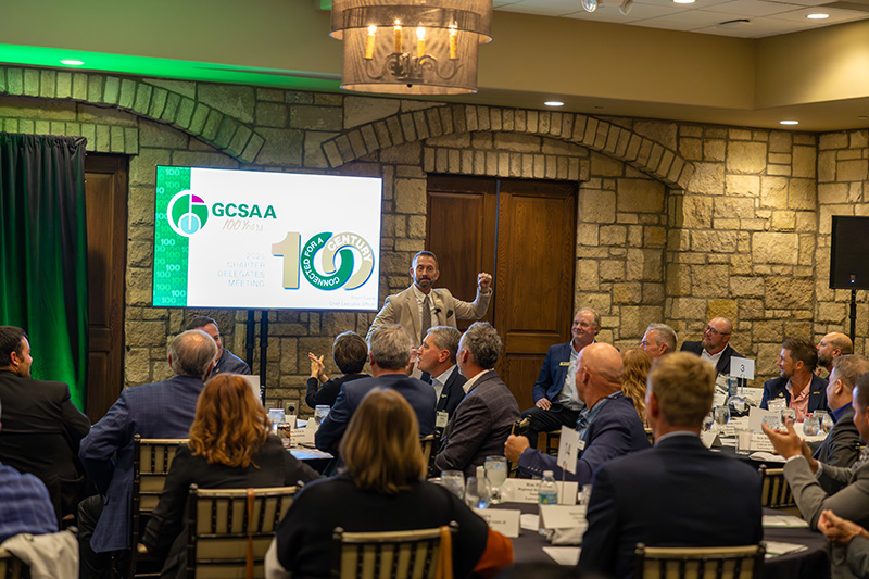 a large group of men sitting inside a hotel conference room in front of a stage with green lighting