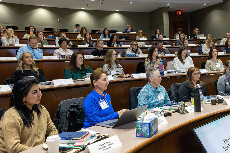Women sitting in chairs in a tiered conference room looking forward