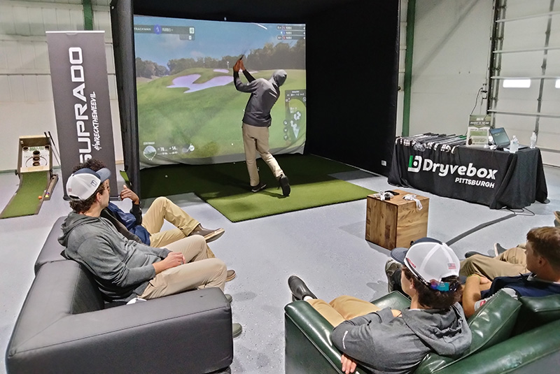 Young men sitting in a maintenance shop with one man using a golf simulator